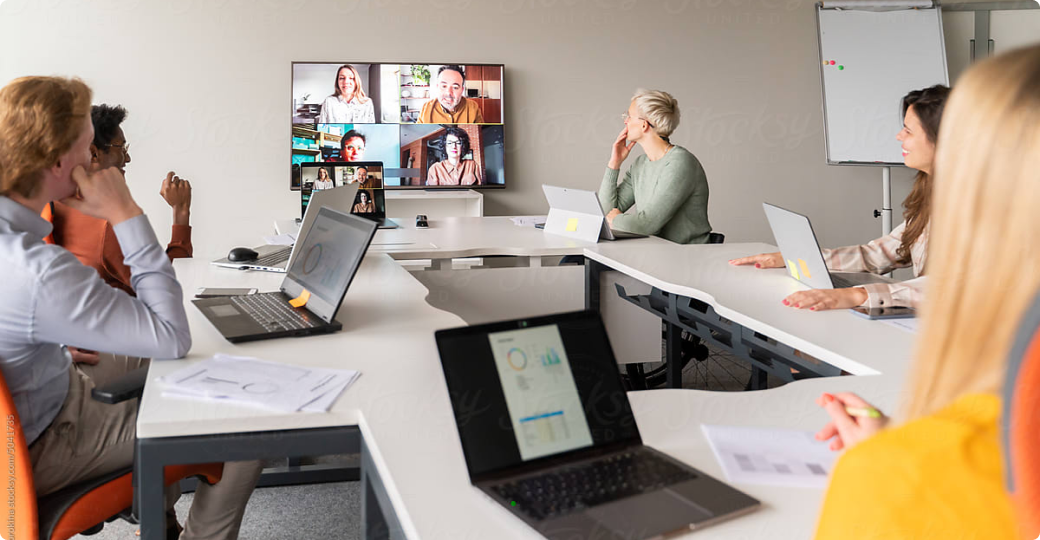 Multiple people at an in-person meeting looking at a screen of people joining the meeting via Zoom.